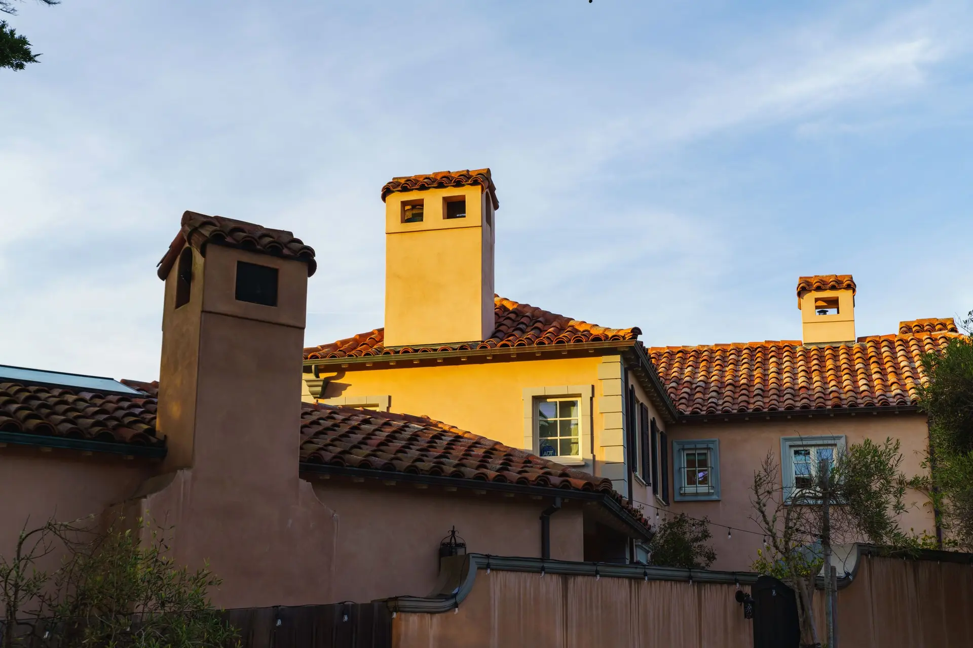 Stucco walls, chimneys and red clay tile roofs in afternoon light