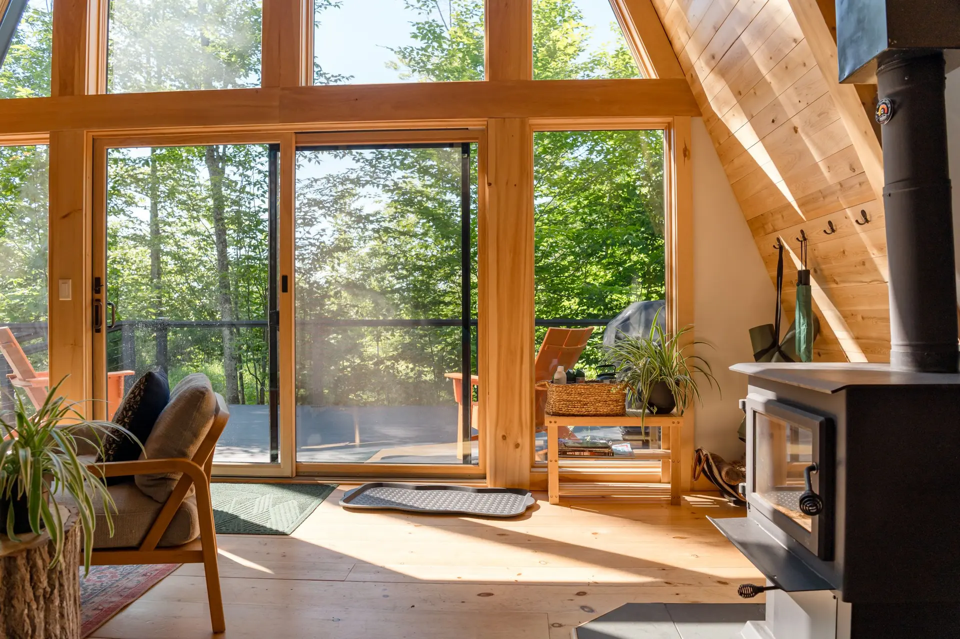 Tall glass doors of a wood cabin opening onto a deck among trees